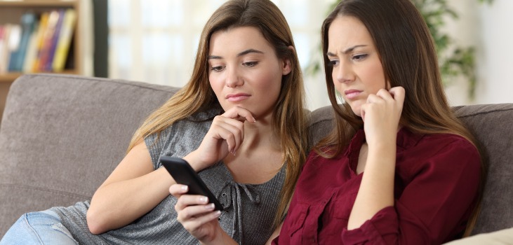 two upset girls looking at their mobile on the couch